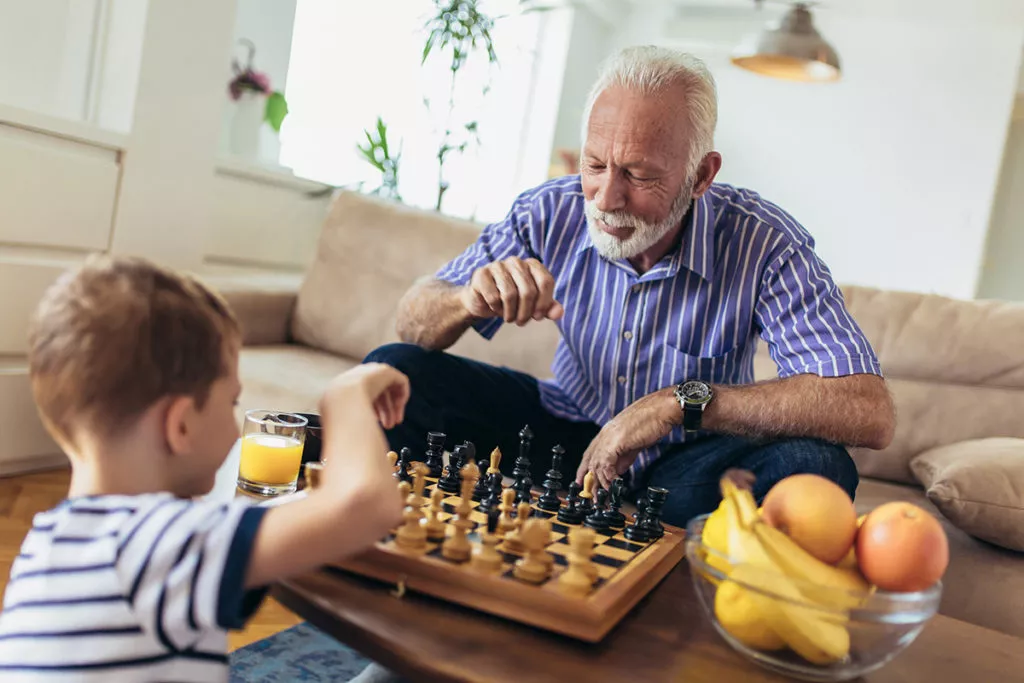Young boy is playing chess with his grandfather at home and learning about critical thinking.