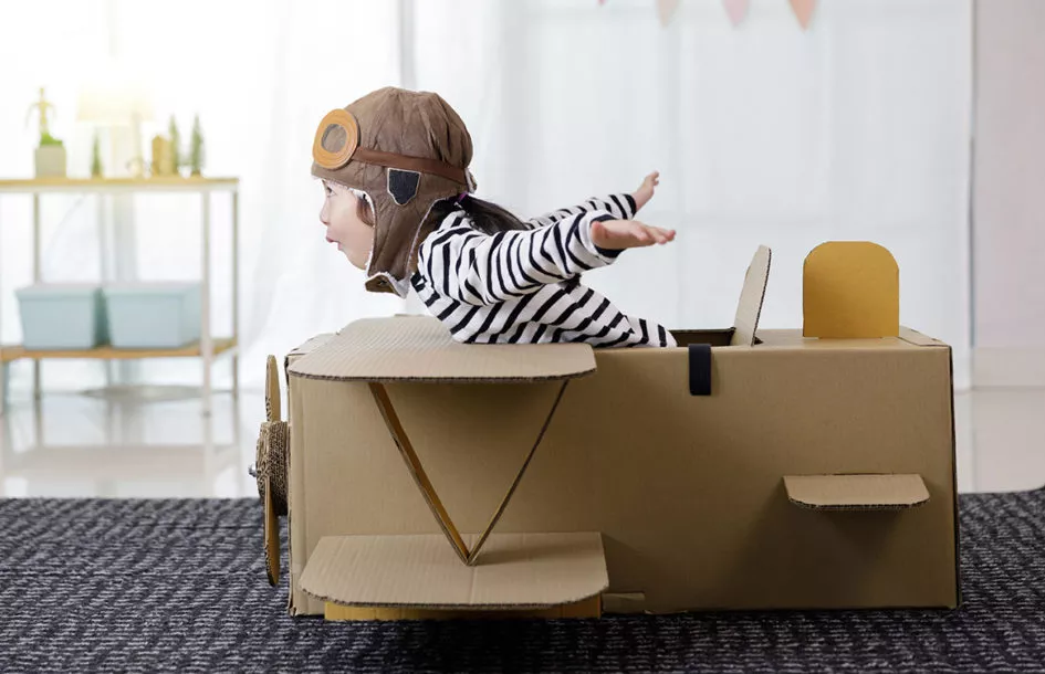 Little girl playing with cardboard toy airplane