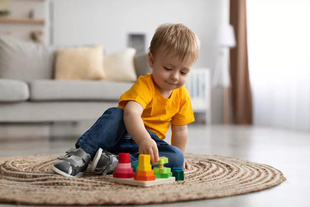 Toddler with wooden colorful stacking and sorting toy learning critical thinking through play.