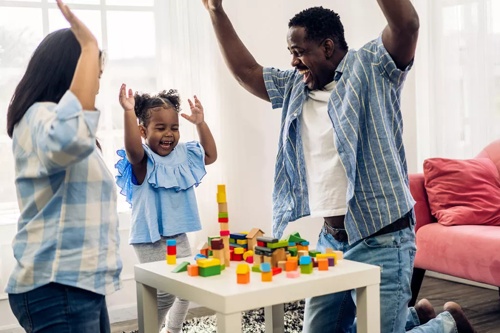 Father and mother with little girl smiling activity learn and skill brain training play with toy build wooden blocks board education game at home.