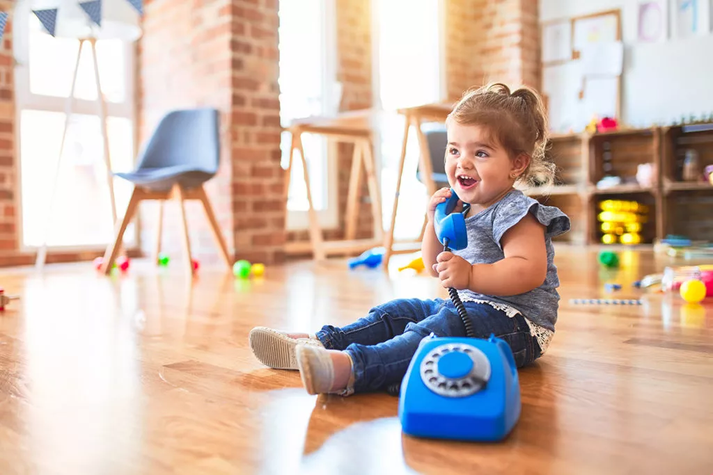 Toddler sitting on the floor and playing telephone to improve language skills through fun activities.