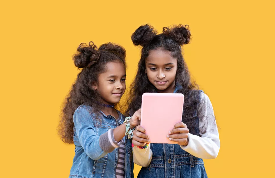 Preschooler girl and school aged girl sharing some learning screen time as recommended by a Rockville day care, center.