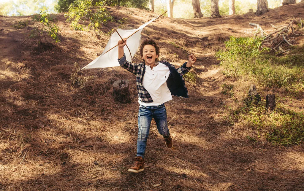 Happy boy running with a kite in hands over his head playing outside as encouraged by the staff at a Rockville Daycare Center.
