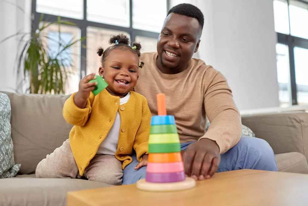 Happy dad playing with toddler daughter with learning toys recommended by Rockville, MD toddler daycare center.