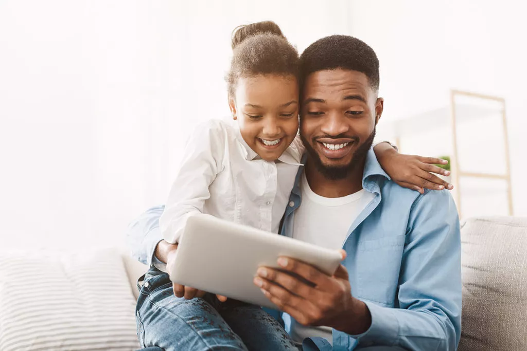 Father teaching daughter to use her tablet for some learning screen time.