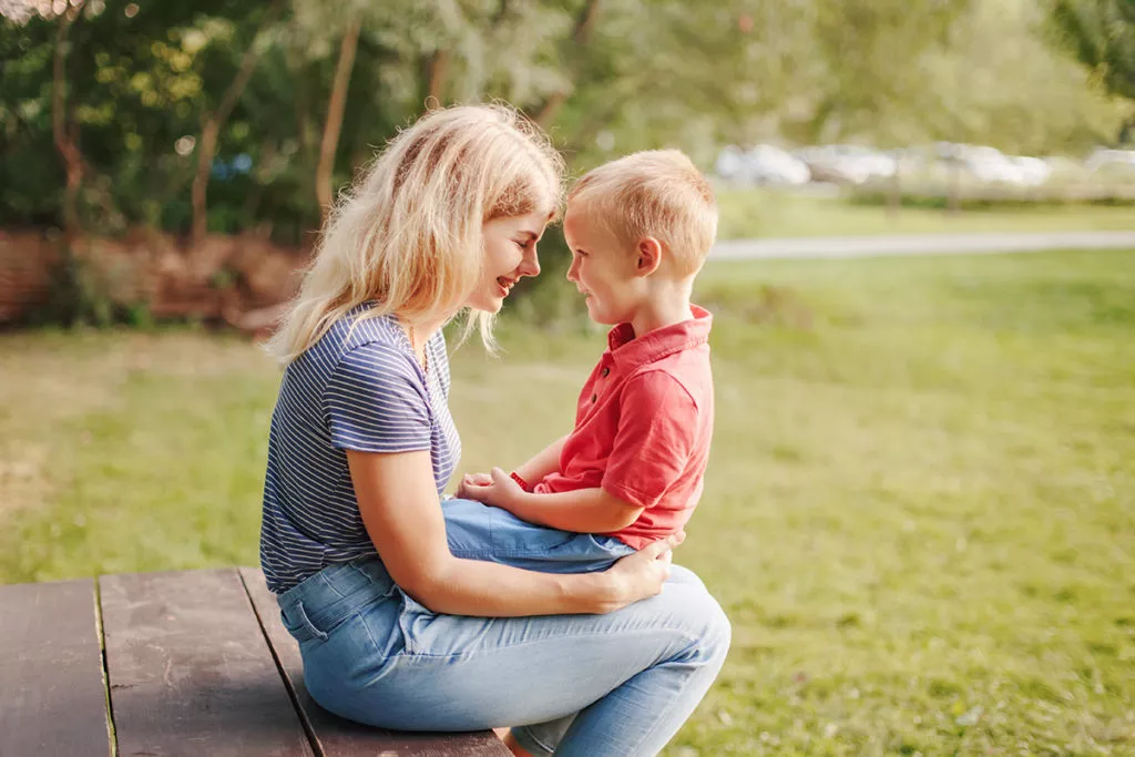 Mother and boy toddler son sitting together face to face outside.
