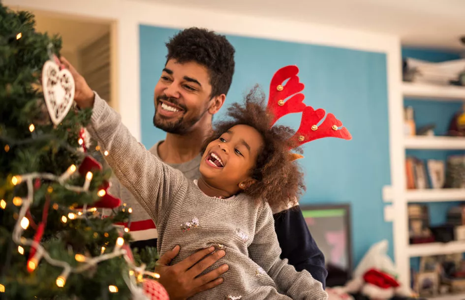 Young girl decorating Christmas tree with dad during a holiday break from school.