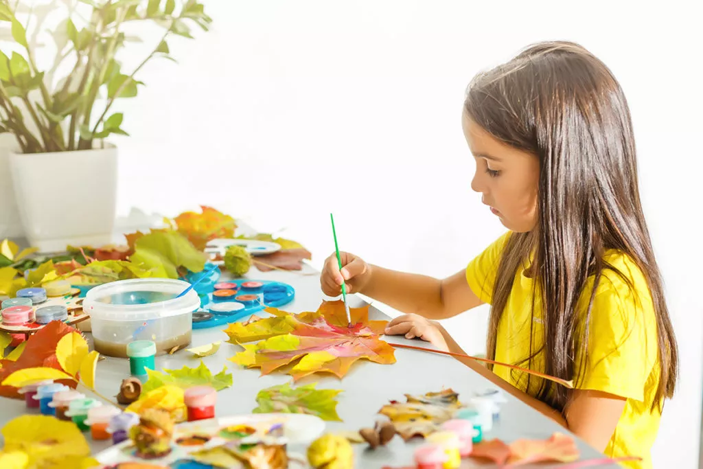 Young girl painting leaves as a fun and easy fall craft activity.