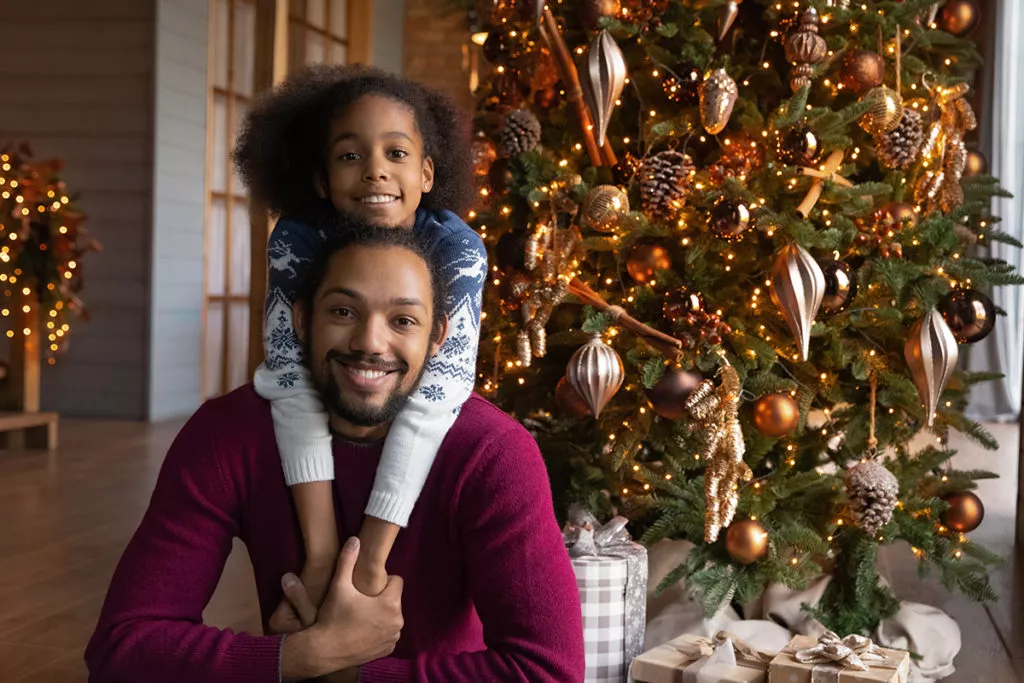 Portrait of a girl hugging her father in front of a Christmas tree during holiday break from school.