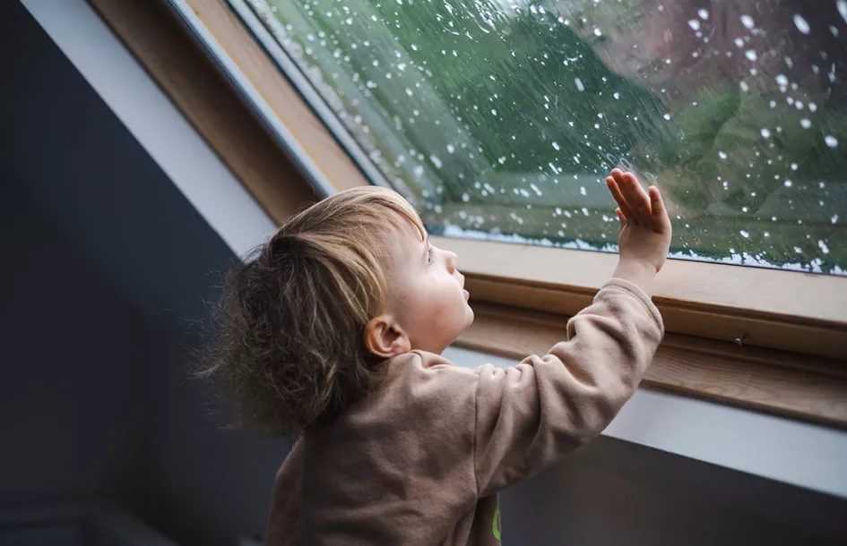 Little preschool boy staying home in bad weather and looking out the window.