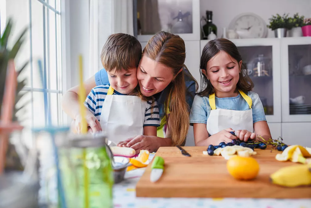 Mother using positive reinforcement to build confidence and recognizing her sons efforts in chopping fruits in the kitchen.