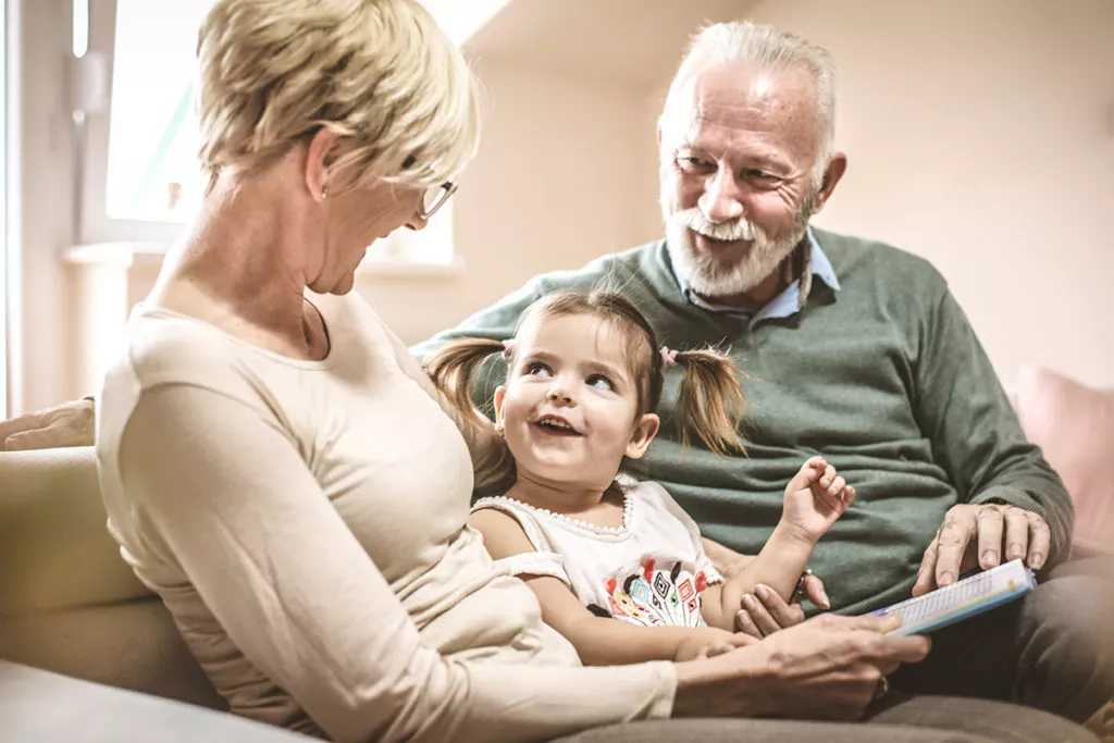 Grandparents reading a book with granddaughter.