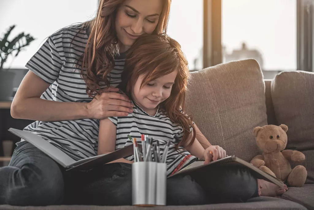 Mother and daughter sitting on the couch and writing creative stories.