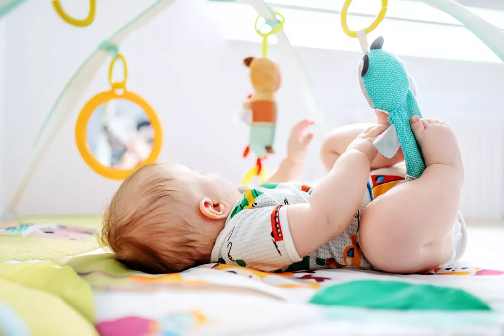 Infant playing on a mat with toys hanging on top at one of the best infant and toddler daycares in MD.