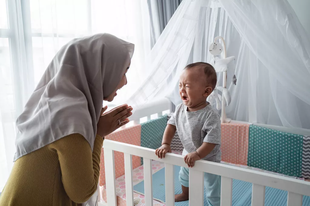 Mother practicing separation with her baby in a crib to work on separation anxiety.
