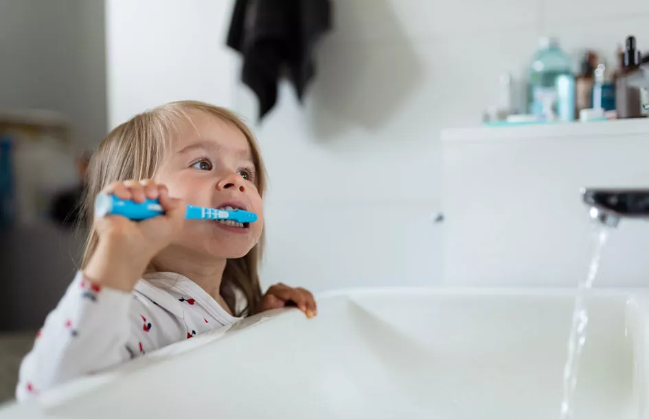 Young girl brushing her teeth in a bright bathroom over the sink.