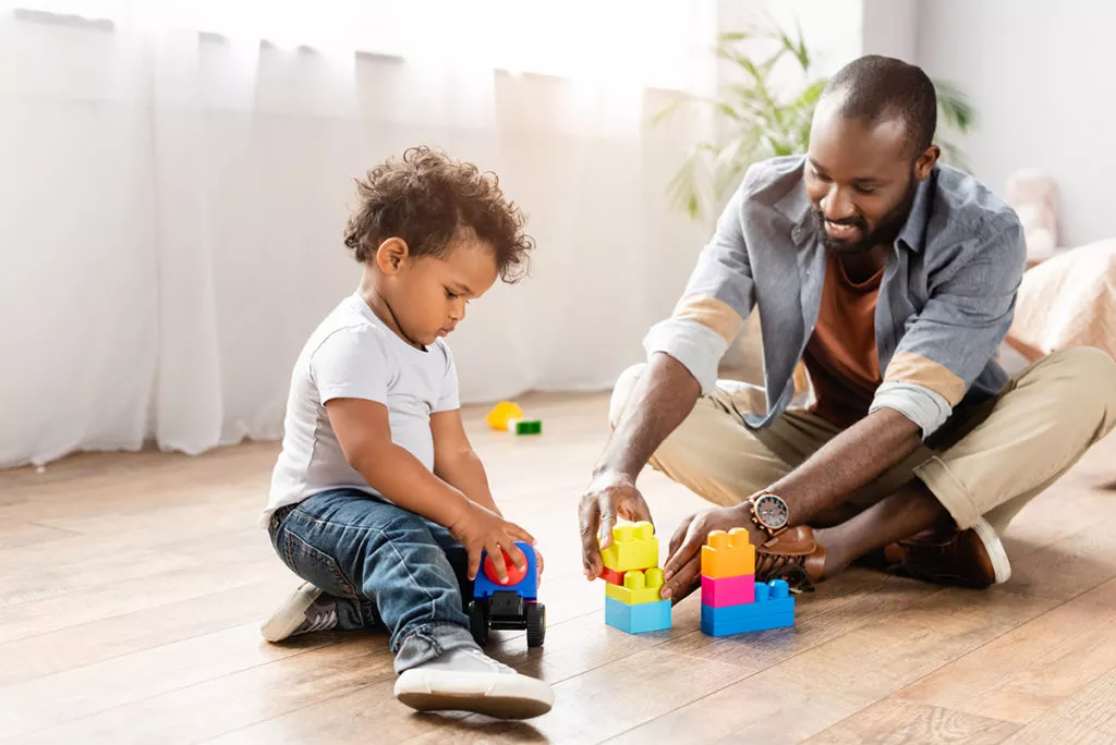 young african american man playing with building blocks on floor with toddler