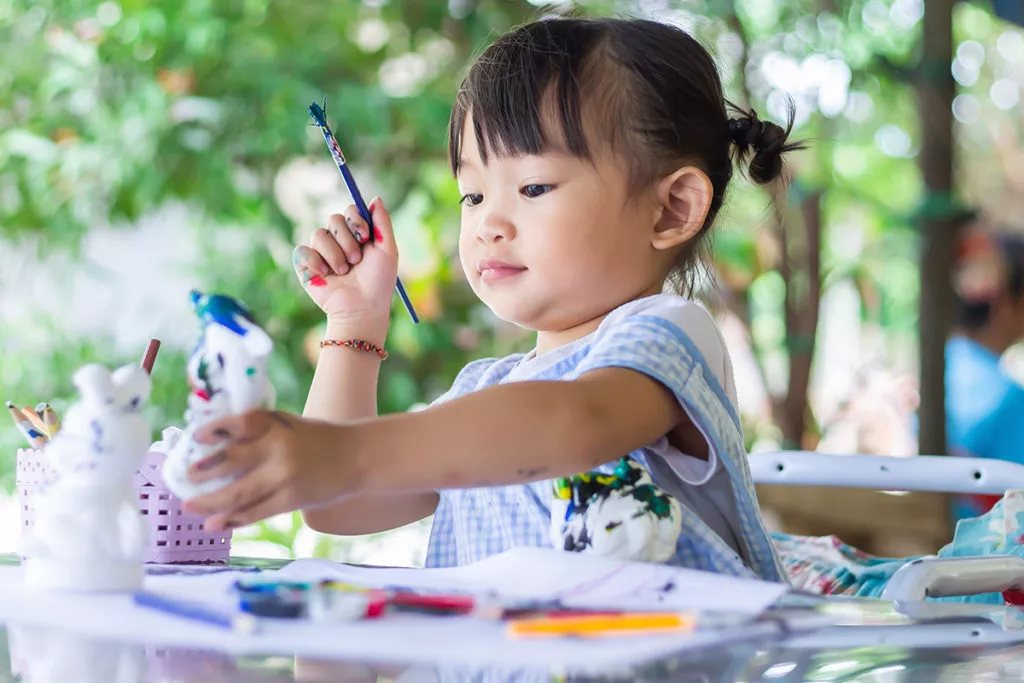 Preschool girl sitting outside and painting.