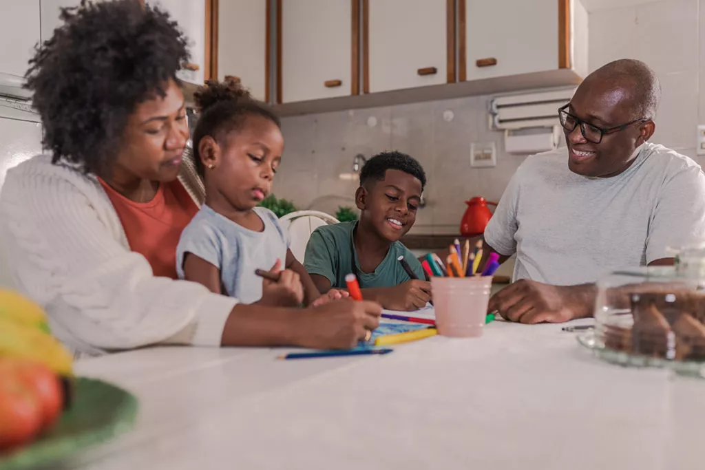 Parents sitting in the kitchen with their kids working on homework as part of a healthy routine.