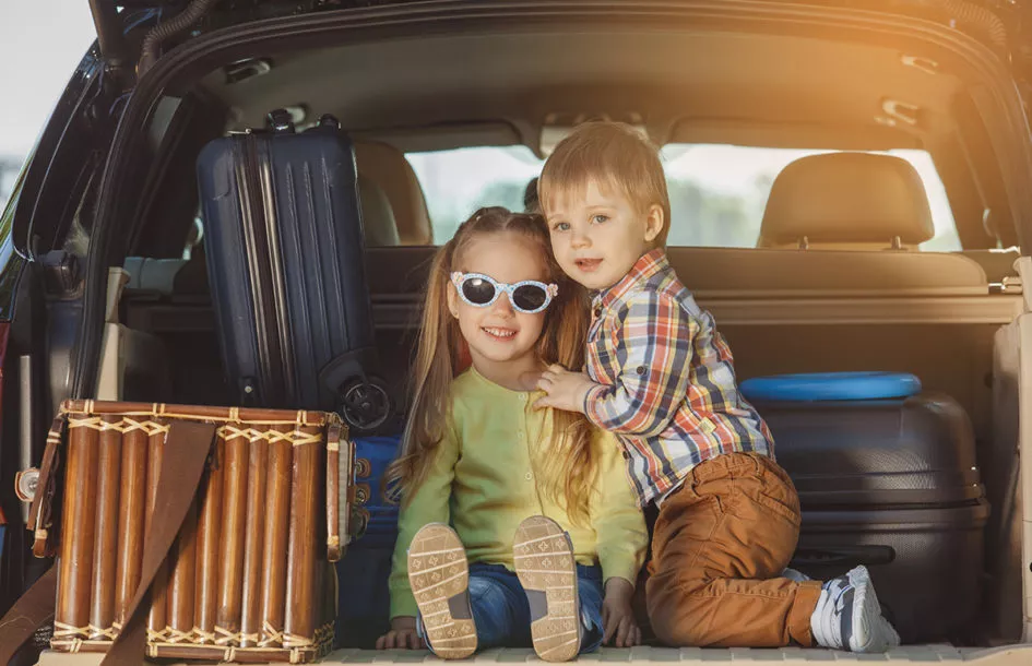 A happy brother and sister sitting in a trunk with all their luggage getting ready to start their family roadtrip.