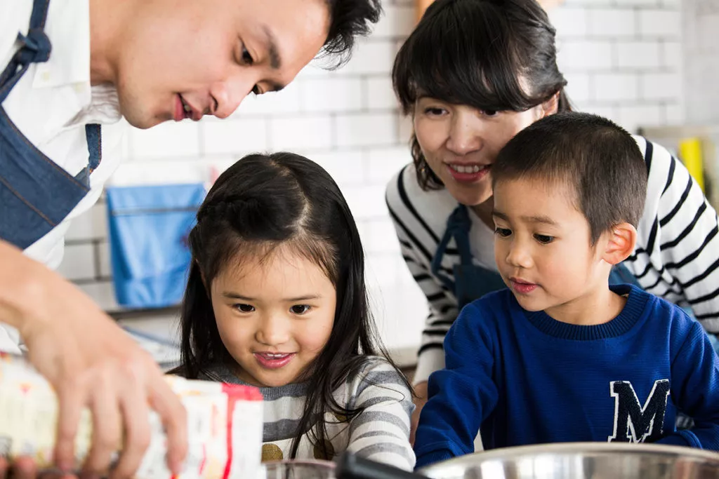 A family with 2 young kids cooking together to show how Cooking with your kids is one of the best ways to use math in real life by measuring the ingredients.