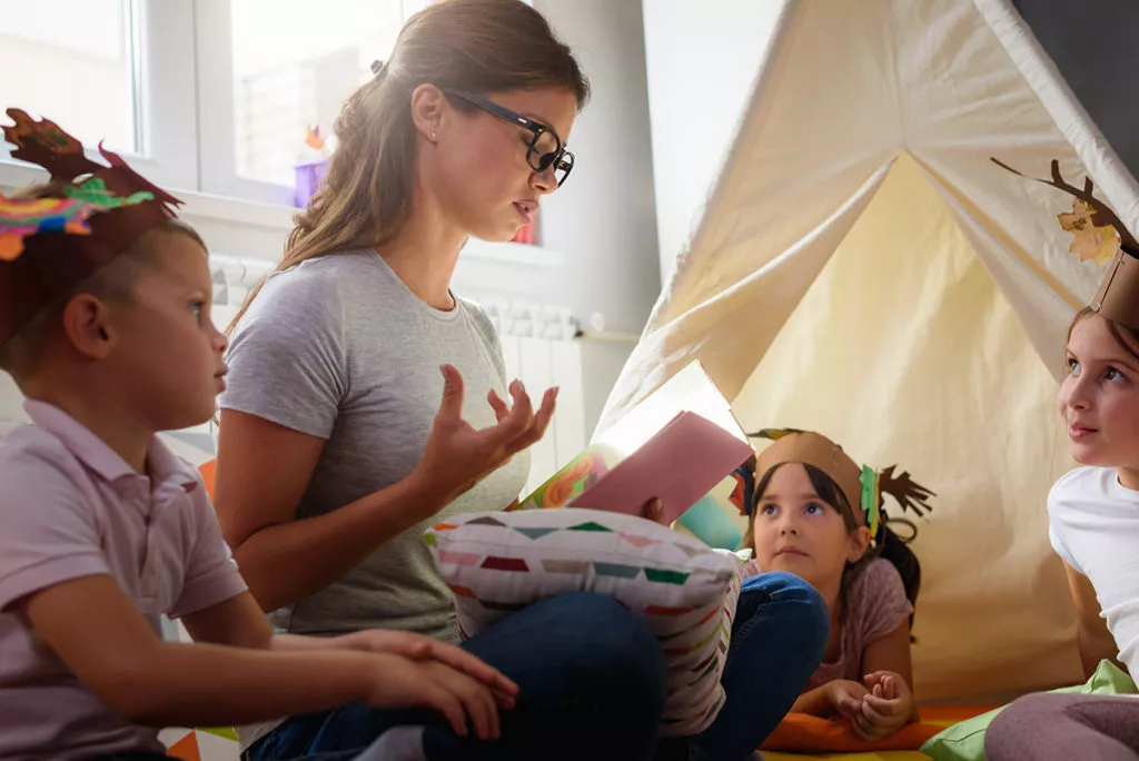 A Teacher at a Preschool in Potomac, MD reading a story to preschool kids to Encourages Active Listening and Clear Speaking.