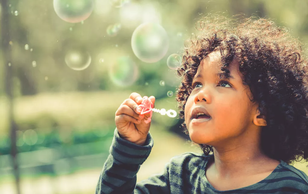 Happy little boy blowing soap bubbles to help build motor skills with everyday activities