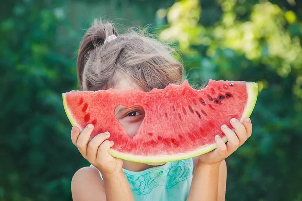 A young girl looking through a hole in her watermelon slice, being silly and having fun at a summer camp in Rockville, MD