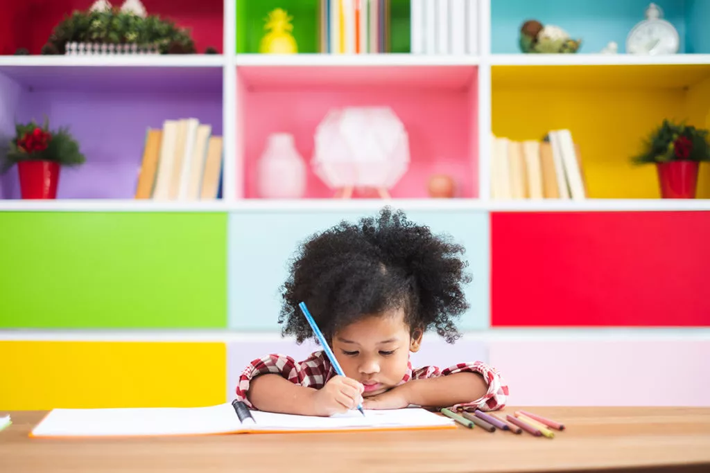 Cute preschool girl sitting at.a table in an Olney, MD preschool and learning how to work independently while practicing writing.