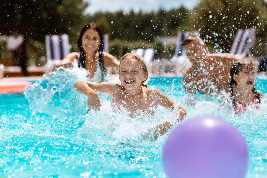Cheerful happy parents and children laughing while playing ball in a swimming pool