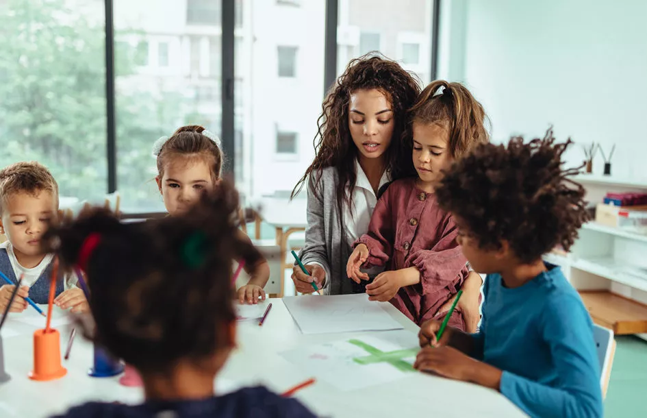 Teacher and preschool children being creative with colorful pencils at a Preschool in Potomac, MD while learning early communication skills.