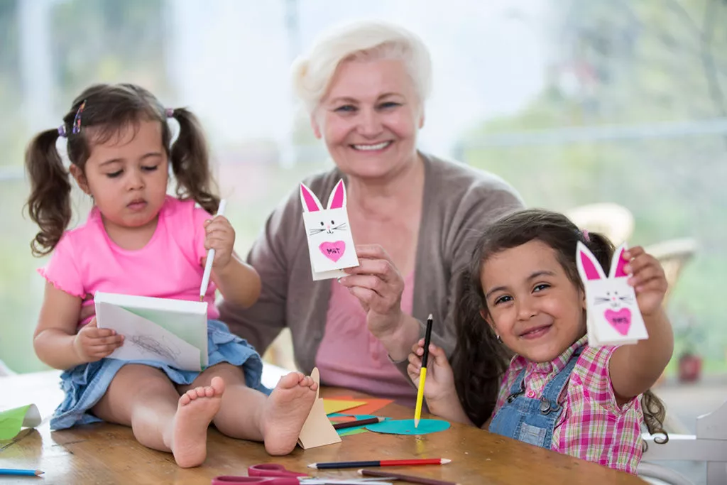 Happy woman showing craft rabbit while sitting with granddaughters at home on a rainy spring day.
