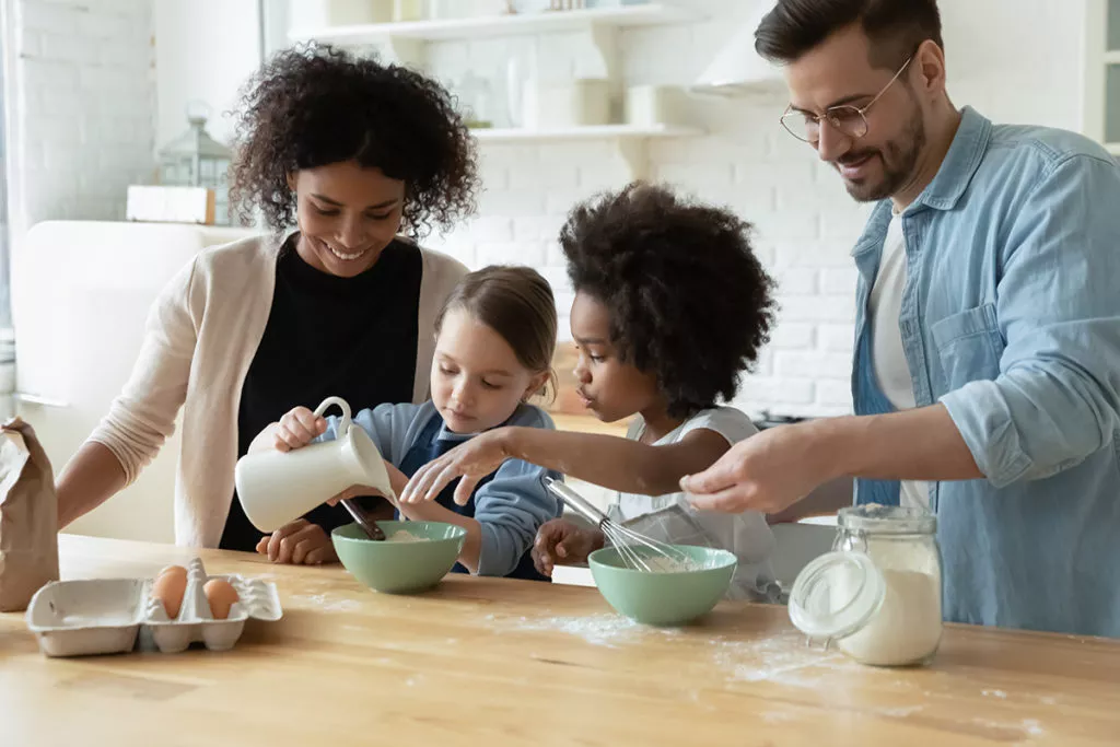 Happy young multiethnic family with little children baking treats in the kitchen together as a fun indoor activity on a rainy spring day.