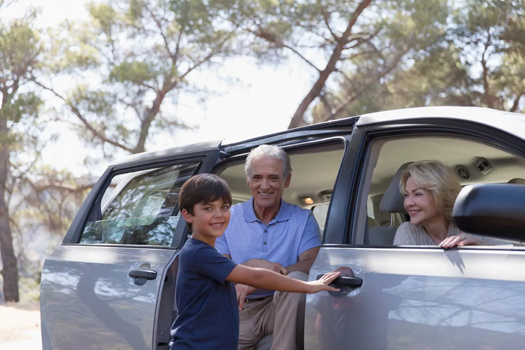 Happy grandparents and grandson next to their minivan, about to start their family roadtrip.