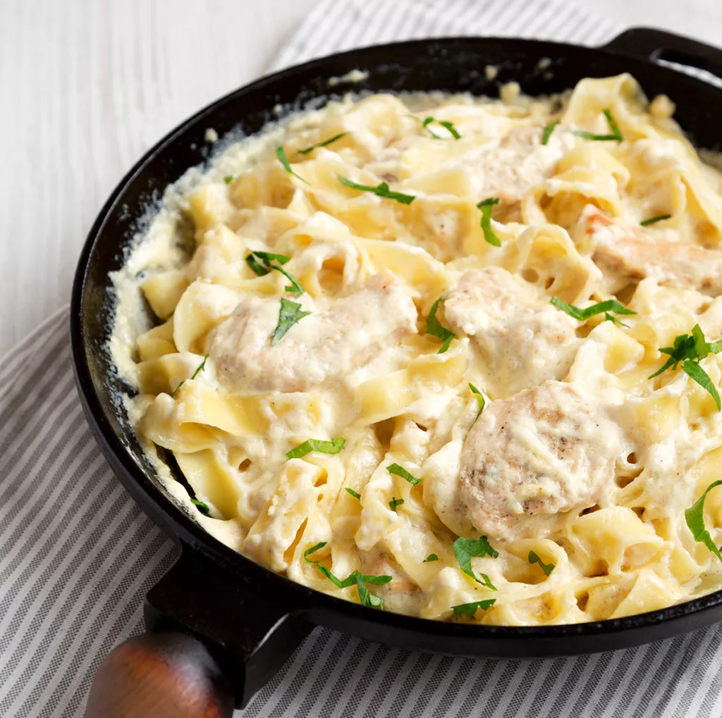 Homemade Chicken Fettuccine Alfredo in a cast-iron pan on a white wooden background, low angle view.