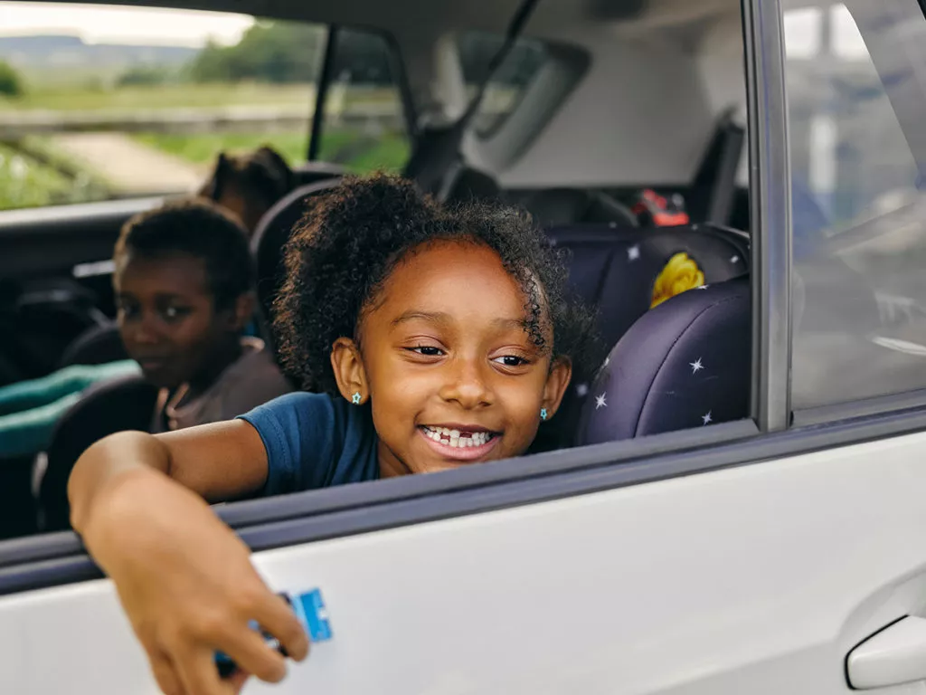 Happy Siblings sitting in the backseat of their family car on a roadtrip.