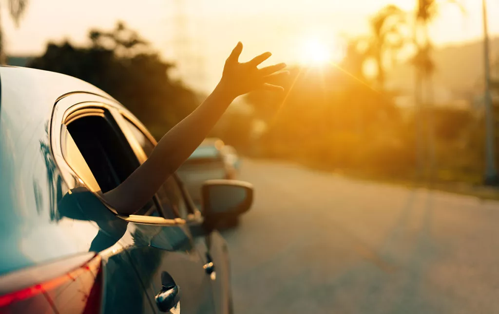 Happy kid riding in the car with family and sticking his hand out with the sunset in the background.