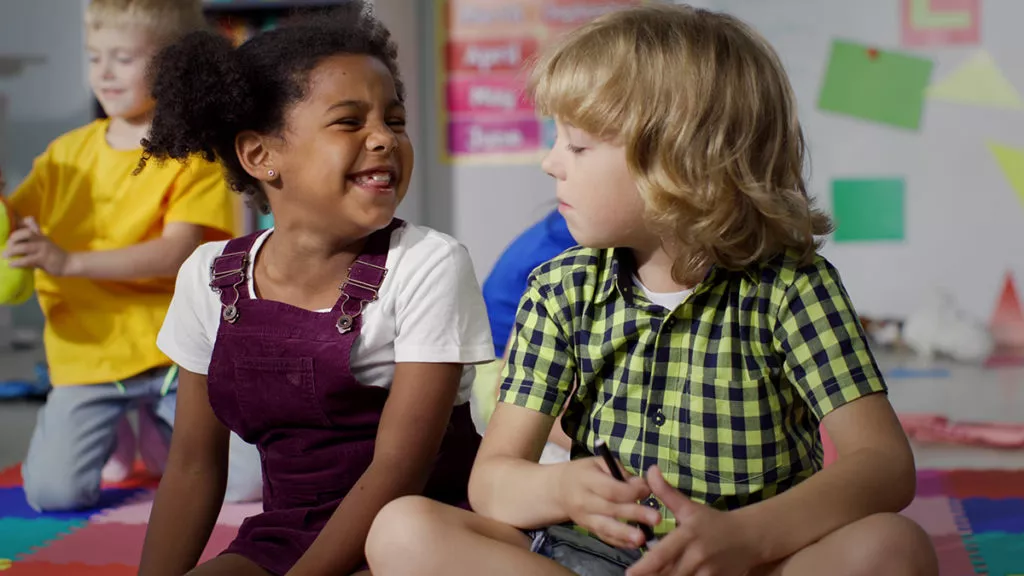 2 preschool kids sitting snd talking on floor at a Rockville Daycare while learning important social skills in preschool.
