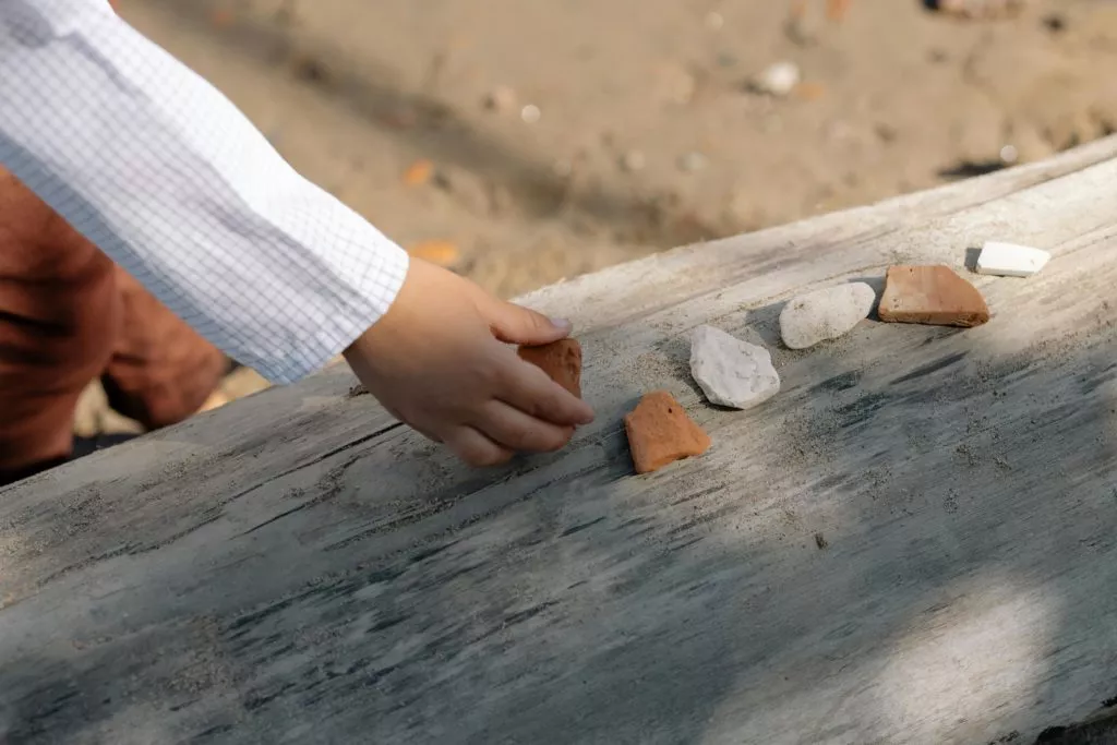 Child playing with different shape rocks on a log on the beach