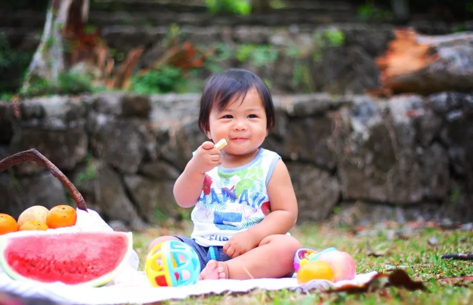 Toddler sitting outside on a sunny summer day, happily eating a slice of watermelon