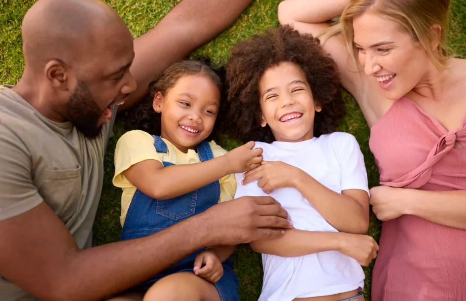 Overhead Shot Of Multi-Racial Family Lying On Grass Tickling Children