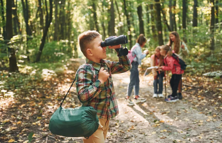 Fun fall nature walk activities for kids: Boy with binoculars standing in front of his friends.