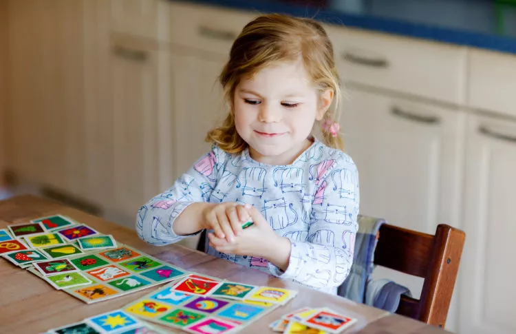 Activities to improve memory in preschoolers: toddler girl playing picture card game.