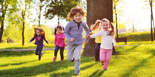 slide many young children smiling running along the grass in the park practicing gross motor skills for children