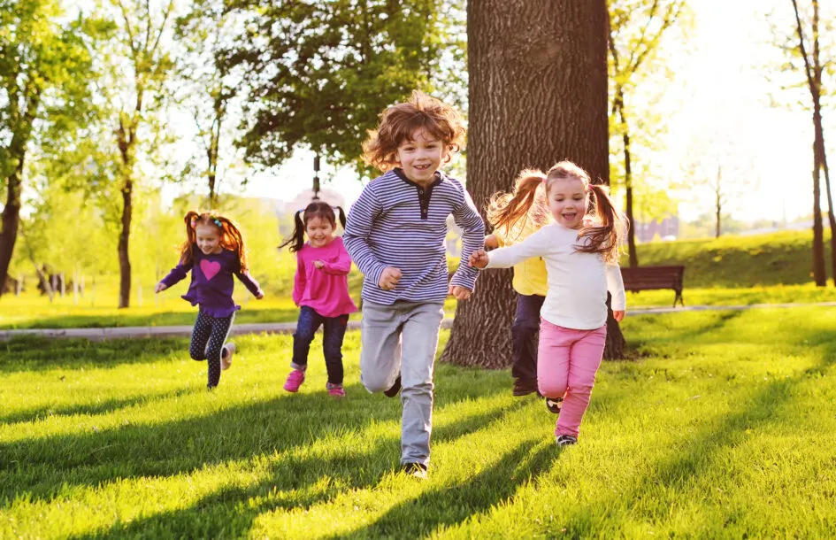 many young children smiling running along the grass in the park practicing gross motor skills for children