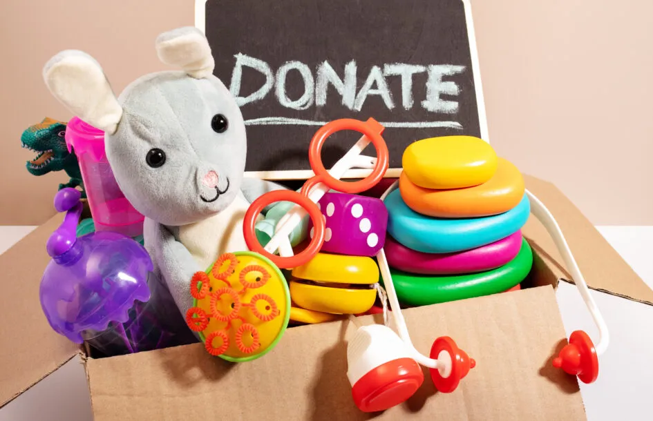 Toys for children in a box with a Donate sign on a blackboard against a beige background, minimal style still life. Holiday volunteering for families