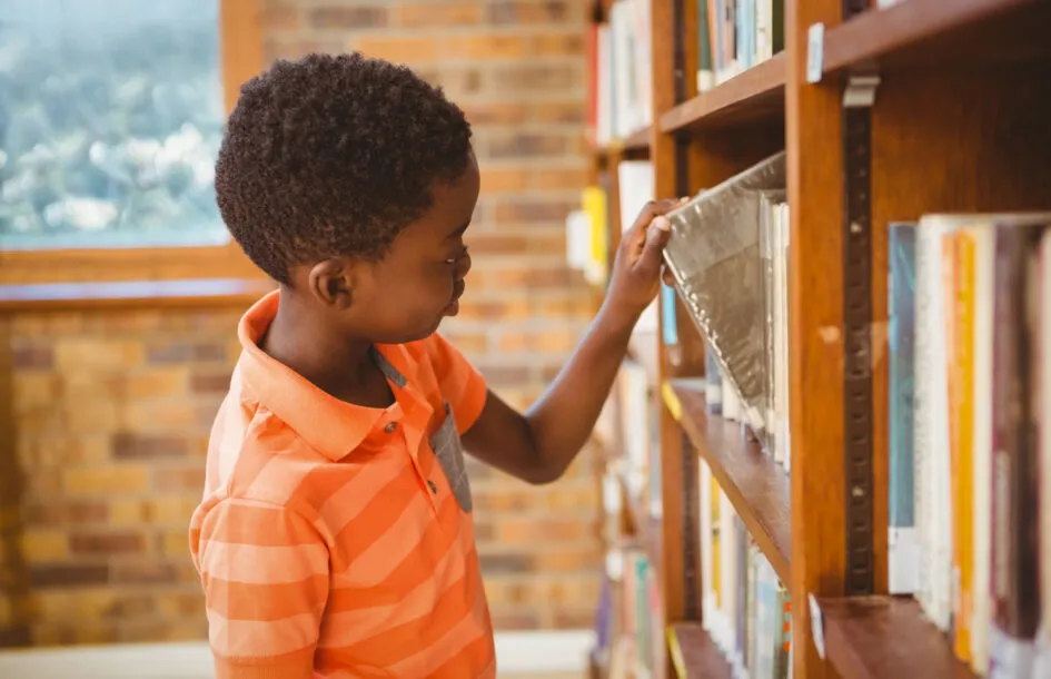 Side view of cute little boy selecting book in the library, encouraging reading in children
