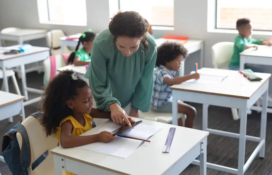 female teacher showing digital tablet to elementary schoolgirl. encouraging independance in children