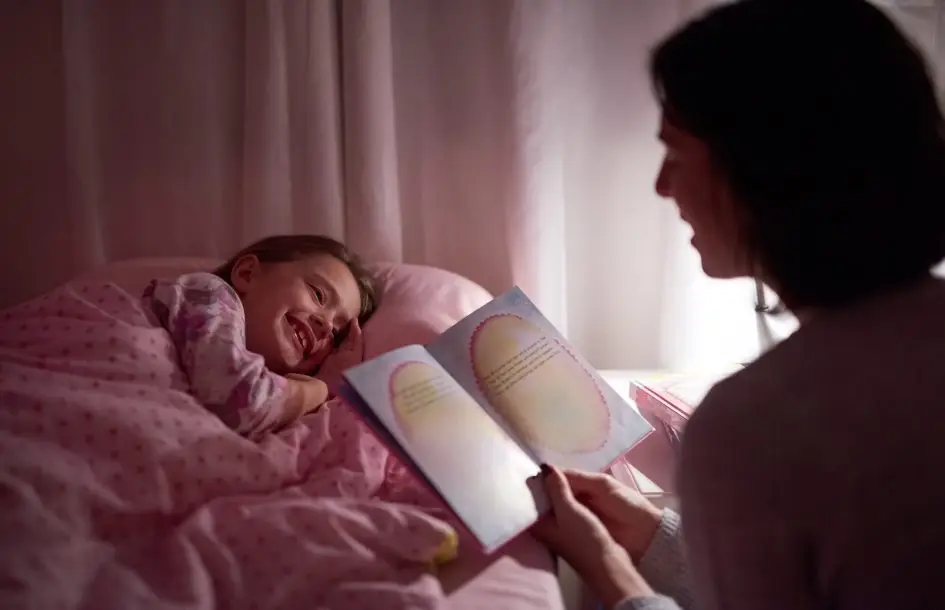 Bedtime story telling ideas for preschoolers: little girl lying in bed while her mom reads a bedtime story.