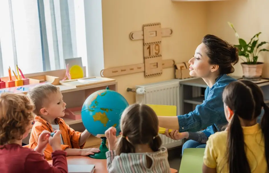 young teacher talking to group of students near a globe for play based learning in silver spring md